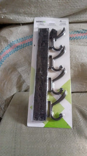 Black four-hook coat rack in its clear plastic packaging with a white and green label, resting on a textured surface.