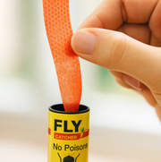A hand pulls an orange, textured sticky strip from a yellow Fly Catcher tube labeled 