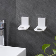 Two white plastic bottle holders with clear adhesive pads lying on a light gray tiled floor beside a white bathtub.