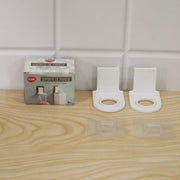 A product box and two white plastic bottle holders with their clear adhesive pads are arranged on a light wooden surface.