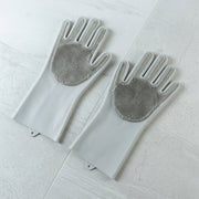 A pair of grey silicone scrubbing gloves with textured palms lays flat on a light grey tiled surface.