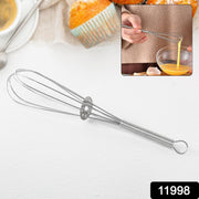 A silver spring coil whisk is displayed on a white surface with a blurred background of baked goods and a person whisking