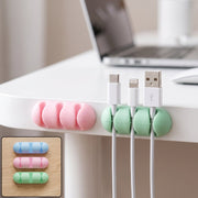 A pink and a green silicone cable organizer are attached to a white desk, holding three charging cables.