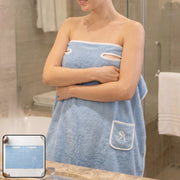 Woman wearing a light blue wearable bath towel with a white trim and a small pocket, standing in a bathroom.