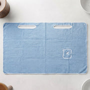 Flat lay of a light blue rectangular bath towel wrap with two armholes and a small pocket with an R monogram.