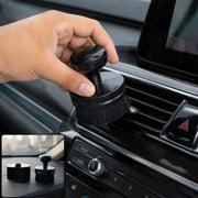 A hand holds a black detailing brush, cleaning a car's air vent, with a small inset showing the brush and its base on a