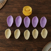 Ten individual petals, five purple and five yellow, arranged in two rows with a yellow flower center on a wooden surface.