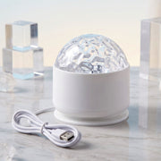 A white LED projection light with a clear textured dome and a white USB cable on a marble surface with clear blocks.