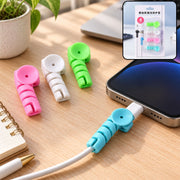 Four colorful spiral silicone cable protectors on a desk, one attached to a phone charging cable.