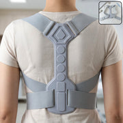 Back view of a person wearing a light gray posture corrector with a rigid central support and elastic straps.