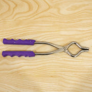 A stainless steel pot lifter with purple handles lying on a light wooden surface.