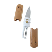 The white and gold multi-tool is disassembled on a light countertop, showing the knife, peeler, and two brown covers.