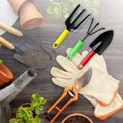 A yellow fork, green cultivator, and red trowel are among various gardening tools and gloves on a wooden surface.