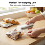 A person uses the white and grey bag sealer to seal a clear bag of dried fruit on a wooden counter.