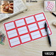 A sheet of 12 red-bordered white writable labels on a wooden desk with a pen, paper clips, and a jar of cookies.