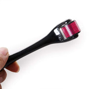 A hand holds a black derma roller with a purple head and red-tipped needles against a white background.