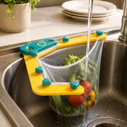 A yellow and blue corner sink strainer holding vegetables under running water in a stainless steel sink.