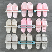 Nine pairs of pink, beige, and gray slippers are organized on three folding racks against a gray tiled wall.