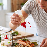 A person drizzles oil from a clear plastic squeeze bottle with a red cap onto salmon and asparagus.