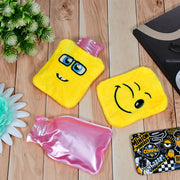 Two yellow emoji hot water bags and one pink plastic hot water bottle are on light wooden surface.