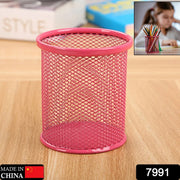 A pink metal mesh pen holder sits on a wooden surface with a blurred background showing a child drawing.