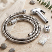 A coiled stainless steel hose, chrome bidet sprayer, wall mount, and screws on a light fabric and stone surface.