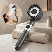 A dark gray shower head with a wide face and rubber bristles, next to a rolled towel, with an inset of a woman showering.