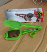 A green plastic slicer with metal blades and a small green square tool rests on a textured surface next to its product box.