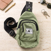 An olive green canvas sling bag with a black strap, Hingham tag, sunglasses, keys, and a pen on a speckled surface.