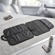 The black car seat protector is unfolded on a gray surface, displaying its padded and mesh sections.