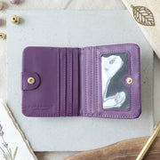 An open purple bifold wallet with multiple card slots and an ID window, lying on a grey surface with decorative beads and a