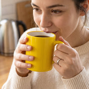 A glossy yellow mug with a white rim and handle is shown against a plain white background.