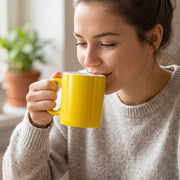 A yellow mug with a white interior stands next to a white box labeled 