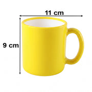 A vibrant yellow mug with a white interior rests on a light-colored, textured surface, with a lemon and books in the