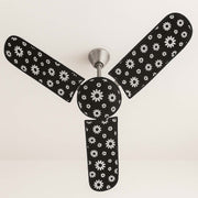 A ceiling fan with black and white floral dust covers on its blades and motor, viewed from below.