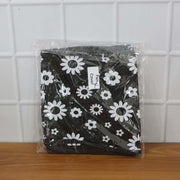 A folded black and white floral fan cover in clear plastic packaging, resting on a wooden surface.