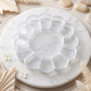 Empty clear flower-shaped plastic organizer box with 13 compartments on a white marble tray with decorative elements.