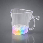 A clear heart-shaped mug with a rainbow-lit base, reflecting on a gray surface.