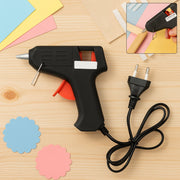 A black and red glue gun with a European plug and cord, with two scalloped paper cutouts and craft paper.