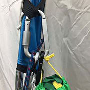 A silver D-ring carabiner with a screw lock is attached to a blue strap, holding ropes and a green bag.