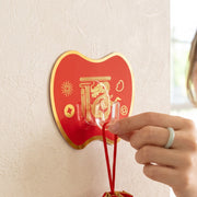 A hand hangs a red drawstring pouch on a red apple-shaped hook with gold Chinese characters and a dragon design. – view 8