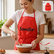 A smiling woman in a white t-shirt and a red Sonifer apron stirs batter in a bowl on a wooden counter