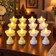 Twelve glowing LED diya candles, six yellow and six white, arranged on a dark wooden table with floral decorations.