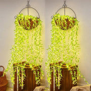Two identical hanging baskets with long strands of green leaf string lights cascading over wooden crates against a light