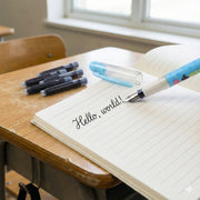 A light blue cartoon animal fountain pen with four black ink cartridges on a wooden school desk.