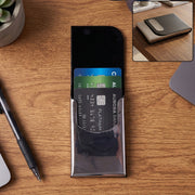 A black leather and steel business card holder on a wooden desk with credit cards inside.