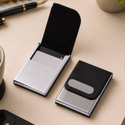 Two black leather and steel business card holders on a beige desk, one open with cards and one closed.