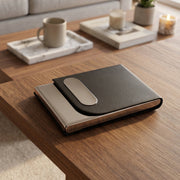 A closed black leather and steel business card holder resting on a wooden coffee table with home decor in the background.