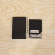 A black box and a black leather and steel business card holder on a light wooden surface.