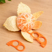 A partially peeled orange sits on a wooden table next to two orange plastic citrus peelers.